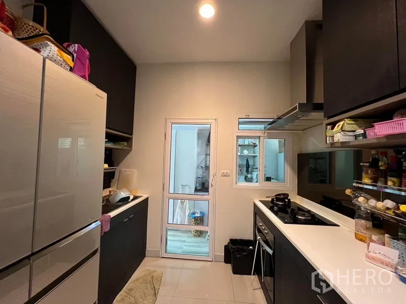 Detached House for rent or sale in Saphan Sung, Bangkok - Enclosed kitchen with black cabinets, gas hob and door to service area.