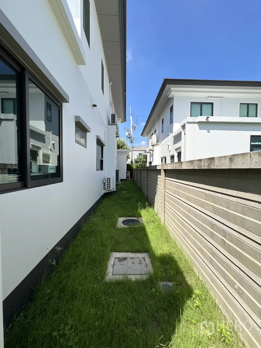 独立式住宅 出租或出售在Mueang Pathum Thani, Pathum Thani - 侧院草带、围墙及室外空调机组。