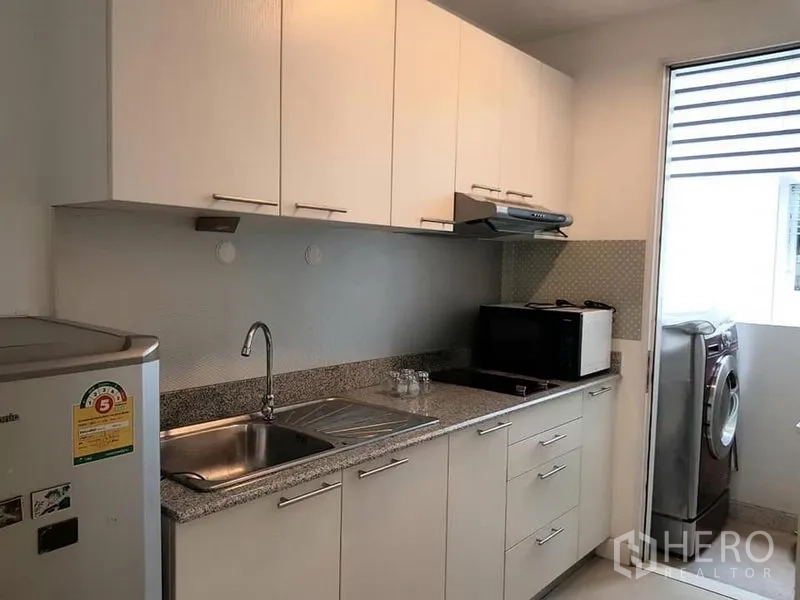 Condominium for rent in Phaya Thai, Bangkok - Separate kitchen with white cabinets, granite countertop, sink, microwave, fridge and a washing machine by the window.
