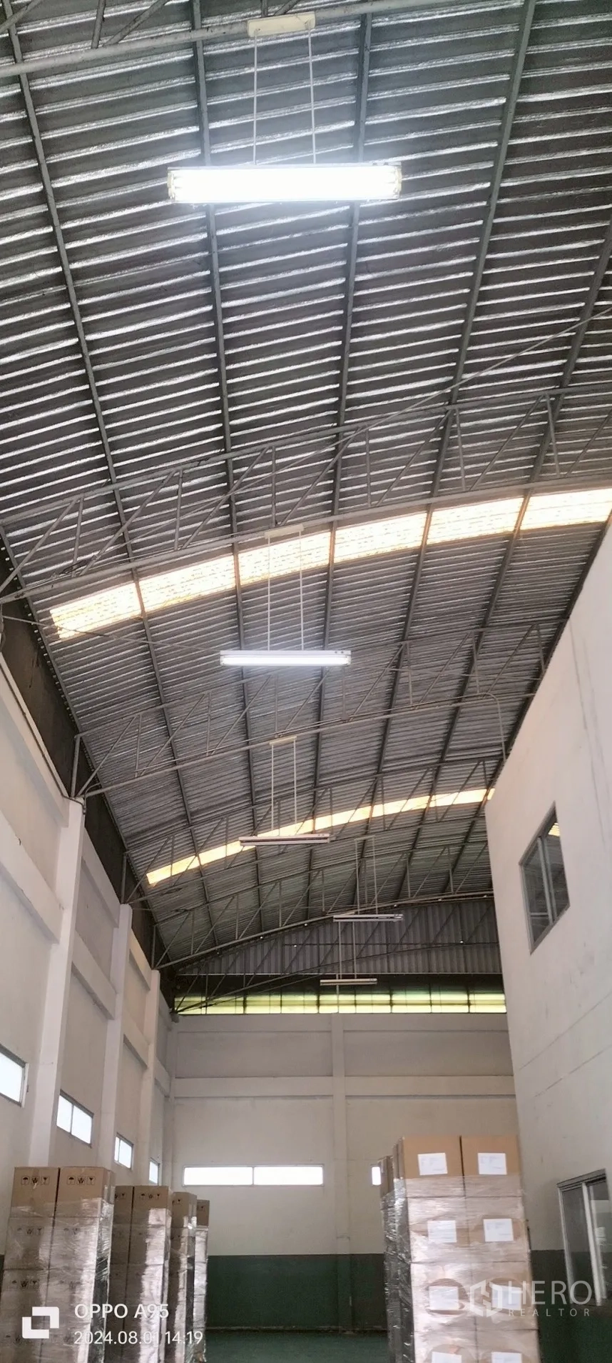 Factory for rent in Khlong Luang, Pathum Thani - Close-up of roof trusses and fluorescent lighting above stored pallets.