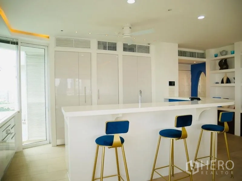Condominium for rent in Khlong Toei, Bangkok - Sleek white kitchen island with three blue-and-gold bar stools.