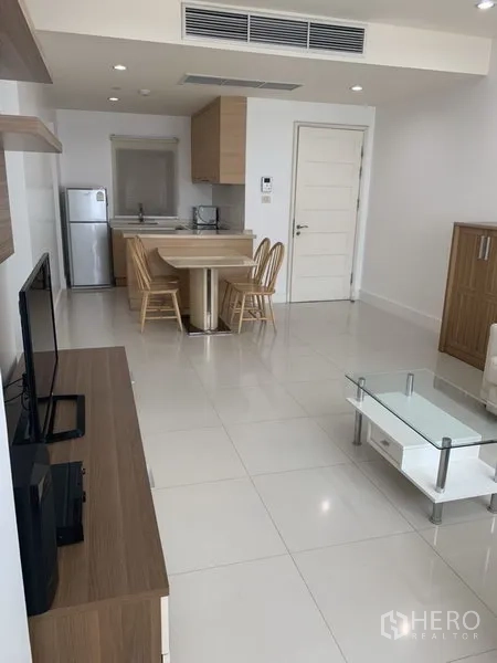 Condominium for rent or sale in Khlong Toei, Bangkok - Bright open-plan living and dining area with modern kitchenette, white tile floors and wood cabinetry.