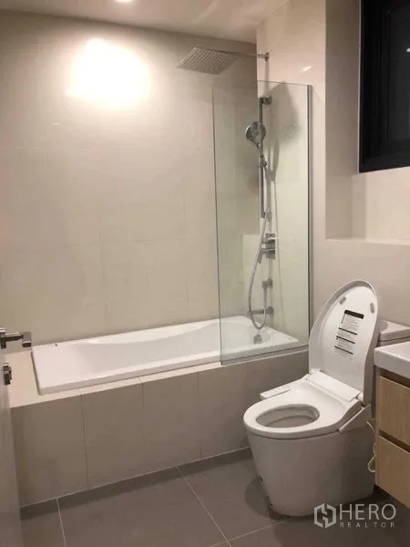 Condominium for rent in Khlong Toei, Bangkok - Bathroom with bathtub, glass shower screen, rain shower, vanity, and toilet.