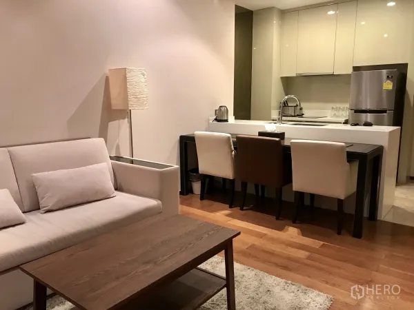 Condominium for rent or sale in Khlong Toei, Bangkok - Open-plan lounge and kitchen with sofa, dining set, island sink and warm hardwood floors.