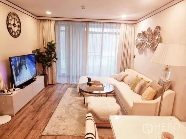 Condominium for sale in Bang Rak, Bangkok - Cozy lounge with area rug, wall art, glass coffee table and large windows draped with sheer curtains.