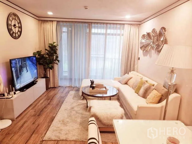 Condominium for sale in Bang Rak, Bangkok - Cozy lounge with area rug, wall art, glass coffee table and large windows draped with sheer curtains.
