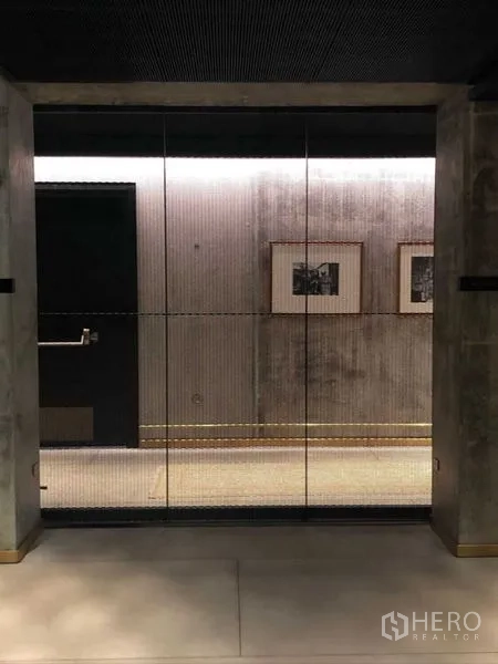 Condominium for rent in Sathon, Bangkok - Industrial-style corridor with glass doors, art on a concrete wall and ambient lighting.