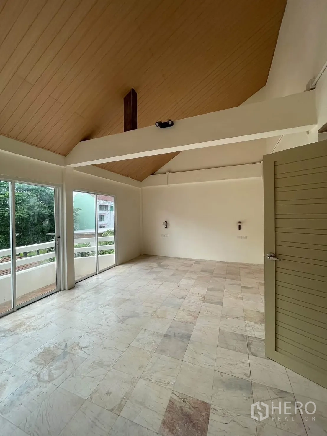 Townhouse for rent in Huai Khwang, Bangkok - Bright living area with vaulted ceiling, exposed beam, tile flooring, and sliding glass doors to a balcony.