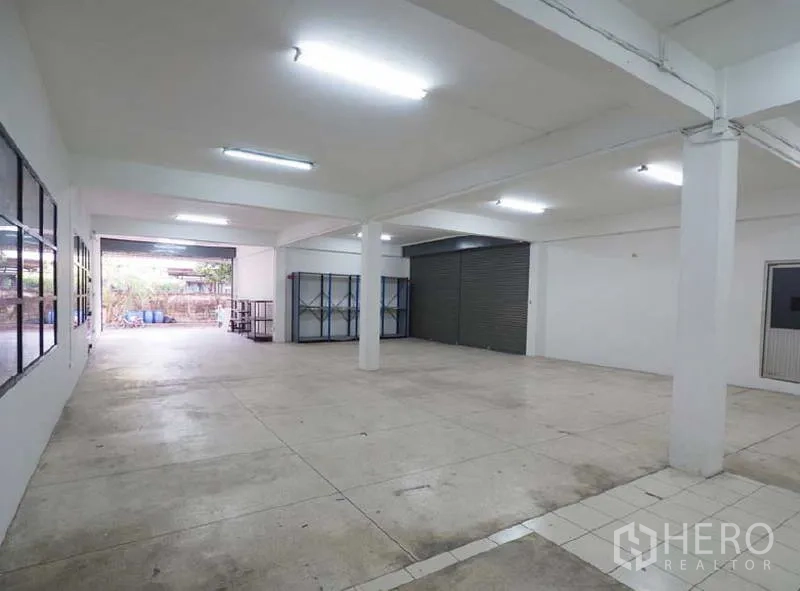 货栈 出租在Bang Kapi, Bangkok - 开放式仓库区，白色立柱、日光灯、混凝土地面及装卸卷闸门。