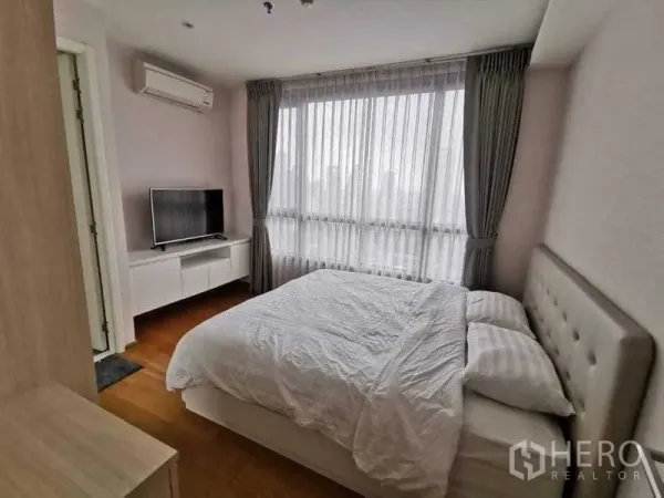 Condominium for rent or sale in Phra Khanong, Bangkok - Primary bedroom with large window, sheer curtains, TV console and air conditioner.