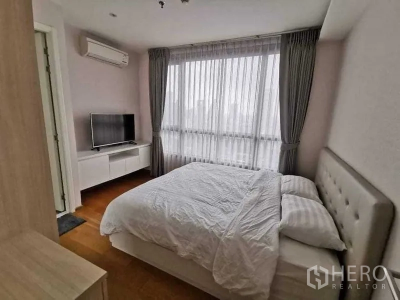 Condominium for rent or sale in Phra Khanong, Bangkok - Primary bedroom with large window, sheer curtains, TV console and air conditioner.