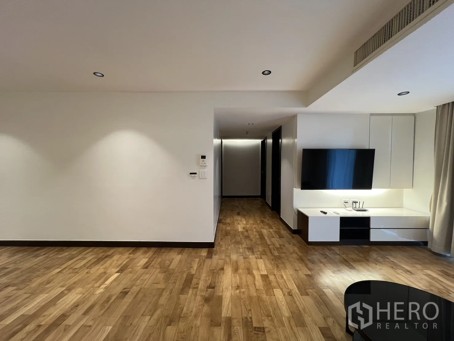 อพาร์ทเมนท์ for rent in Watthana, Bangkok - มุมมองห้องนั่งเล่นเห็นตู้ทีวี ไฟดาวน์ไลท์ พื้นไม้ และโถงทางเดินไปยังห้องต่างๆ