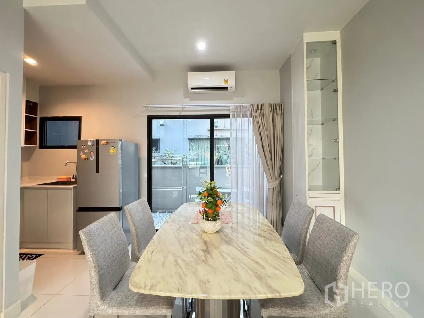 Townhouse for rent in Saphan Sung, Bangkok - Marble dining table with upholstered chairs facing sliding doors to the patio.