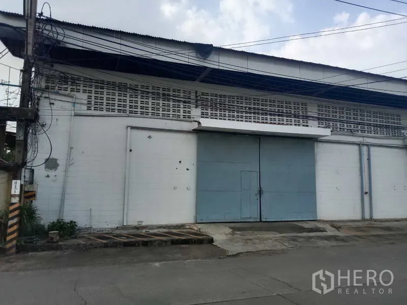 Factory for rent in Samut Prakan - Street-facing facade with large steel door, ramp, and ventilation block walls.