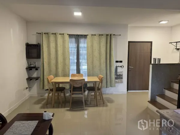 联排别墅 出租在Suan Luang, Bangkok - 明亮的用餐区，木质餐桌四把椅子，窗帘与边角置物架，靠近入户门。
