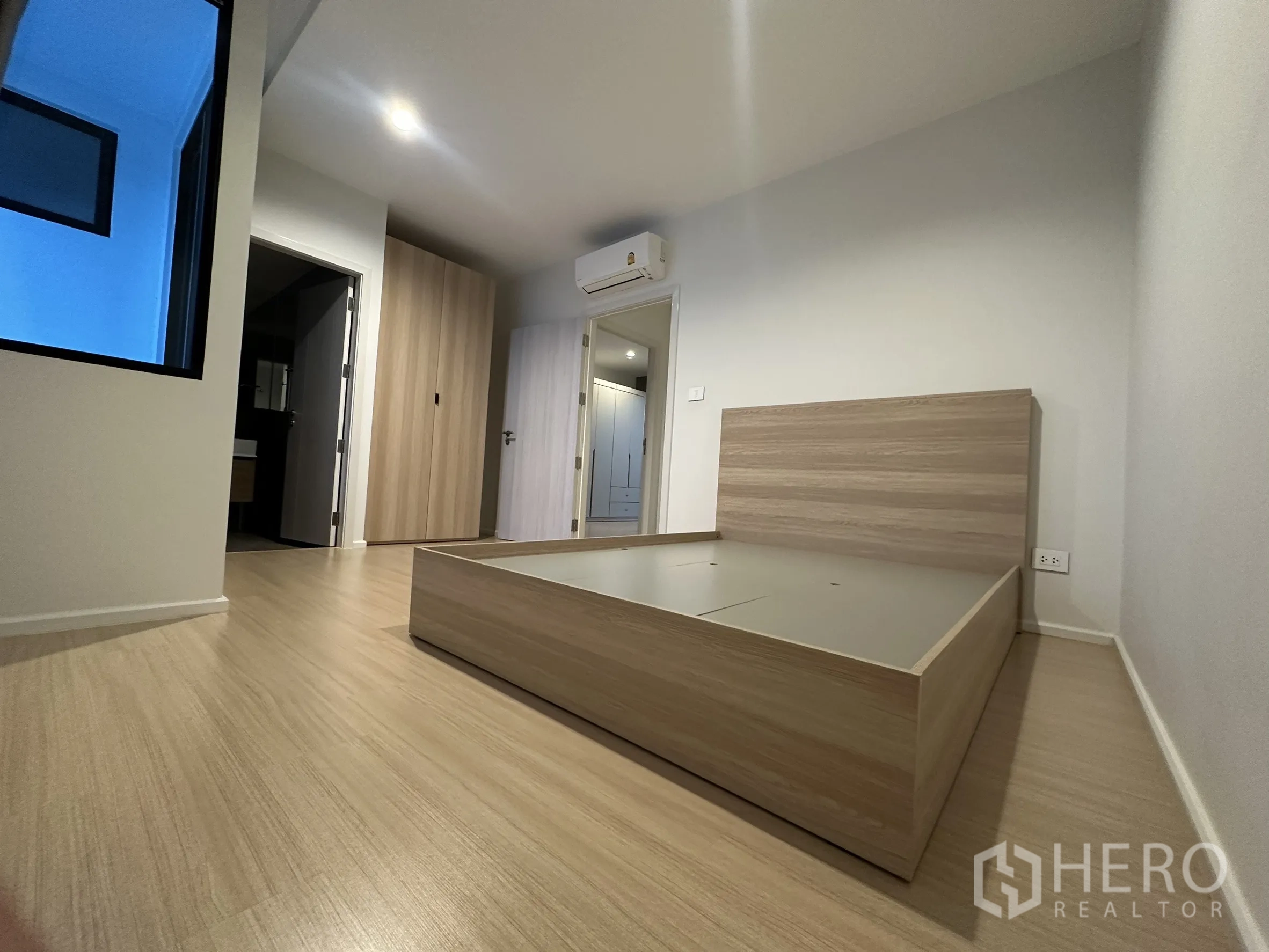 Townhouse for rent in Suan Luang, Bangkok - Bedroom with low bed base, wood floors, built-in wardrobe and wall AC unit.