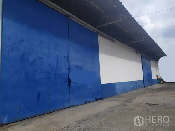 คลังสินค้า ให้เช่าในMueang Samut Prakan, Samut Prakan - ด้านนอกโกดัง ประตูเหล็กบานเลื่อนสีฟ้าขนาดใหญ่ มีหลังคาคลุมลานโหลดและทางรถบรรทุกกว้าง