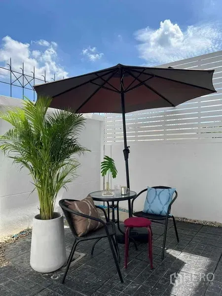 Townhouse for rent in Phra Khanong, Bangkok - Private patio with umbrella, outdoor table and chairs, potted palm and white privacy fence.