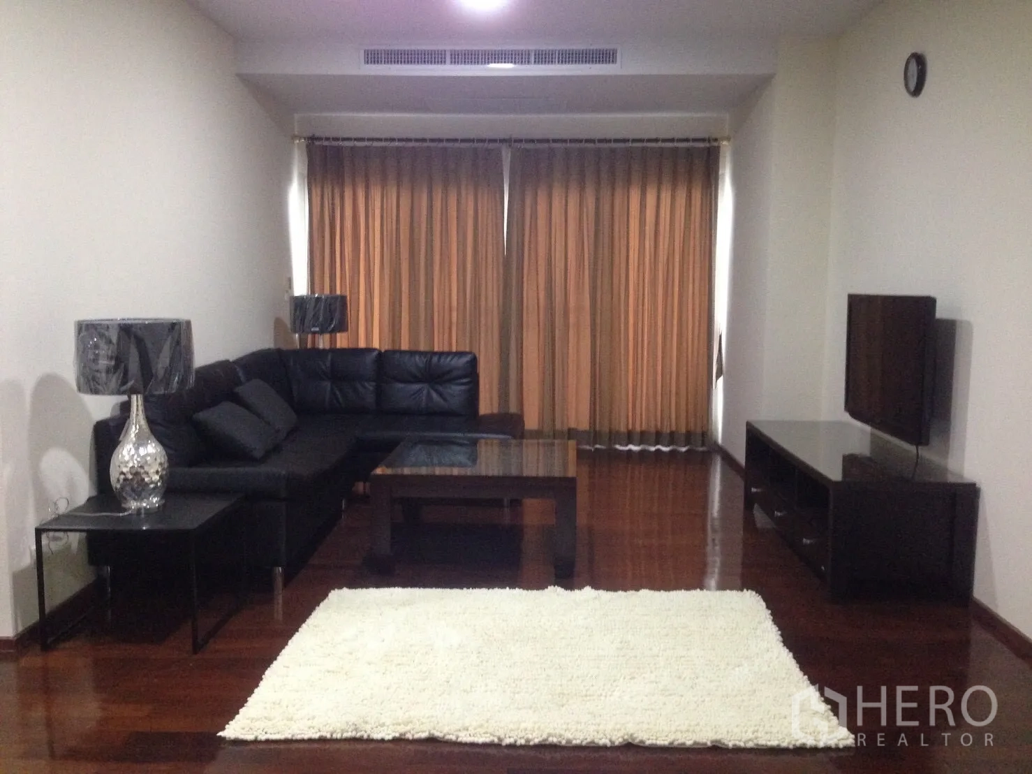 公寓 出租在Watthana, Bangkok - 客厅配L形黑色皮沙发、电视柜与大窗帘。