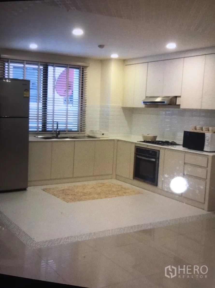 Condominium for rent in Bang Rak, Bangkok - Kitchen view with stainless refrigerator, ample cabinetry and window blinds letting in light.
