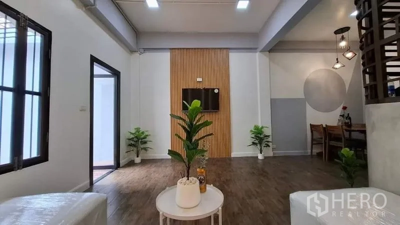 联排别墅 出租或出售在Chatuchak, Bangkok - 起居室带木格电视背景墙、绿植与用餐角，木地板
