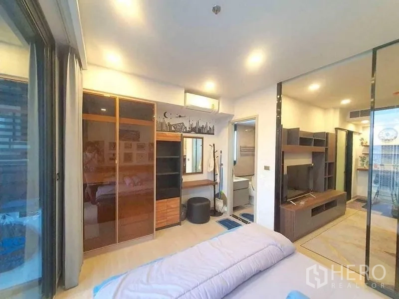 Condominium for rent or sale in Huai Khwang, Bangkok - Bedroom with wardrobes, dressing table, and sliding glass door to living room.