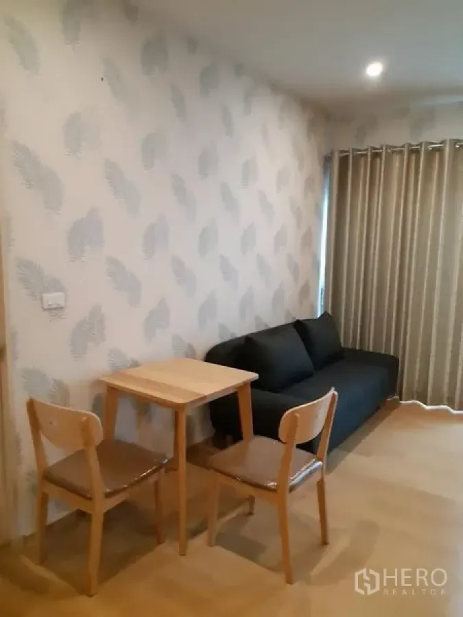 Condominium for rent in Phaya Thai, Bangkok - Dining corner with a small table and two chairs beside a dark sofa and full-height curtains.