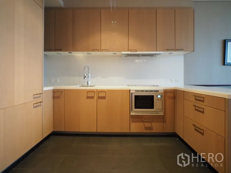 Condominium for rent in Sathon, Bangkok - U-shaped kitchen with light wood cabinetry, built-in cooktop and microwave.