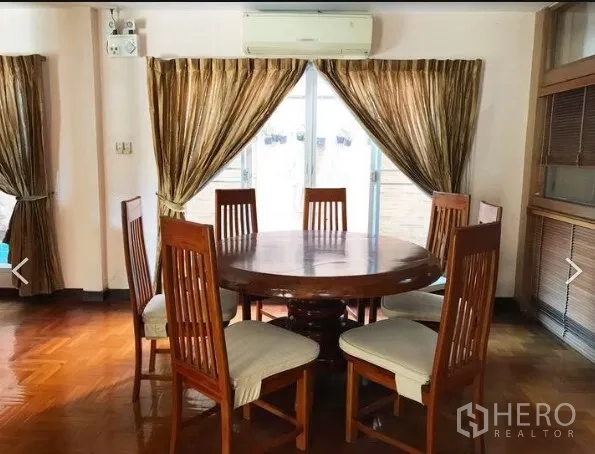 Detached House for sale in Saphan Sung, Bangkok - Dining area with round wooden table and six chairs beside curtained sliding doors.