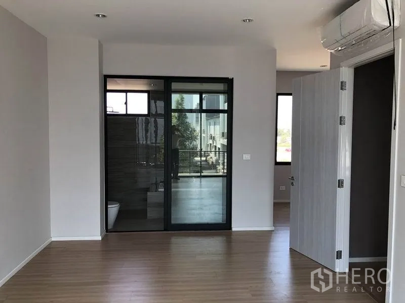 Townhouse for rent or sale in Saphan Sung, Bangkok - Bright bedroom with wood flooring, sliding glass door to an ensuite bathroom and air conditioner.