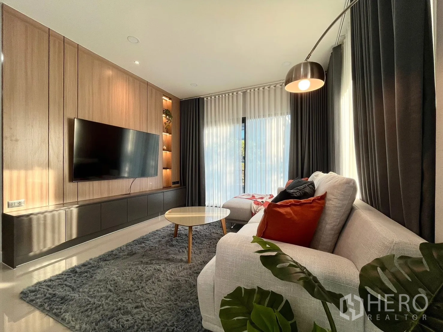 Detached House for rent in Bang Phli, Samut Prakan - Ground-floor living room with L-shaped sofa, wall-mounted TV, and tall curtains.