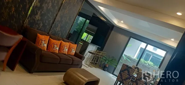 Detached House for rent or sale in Khan Na Yao, Bangkok - Open-plan living and dining area with brown sofa, bar counter and sliding glass doors to garden.