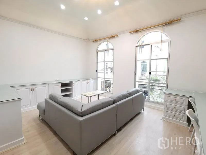 Townhouse for rent or sale in Yan Nawa, Bangkok - Bright living room with arched French windows, built-in cabinets and an L-shaped sofa.