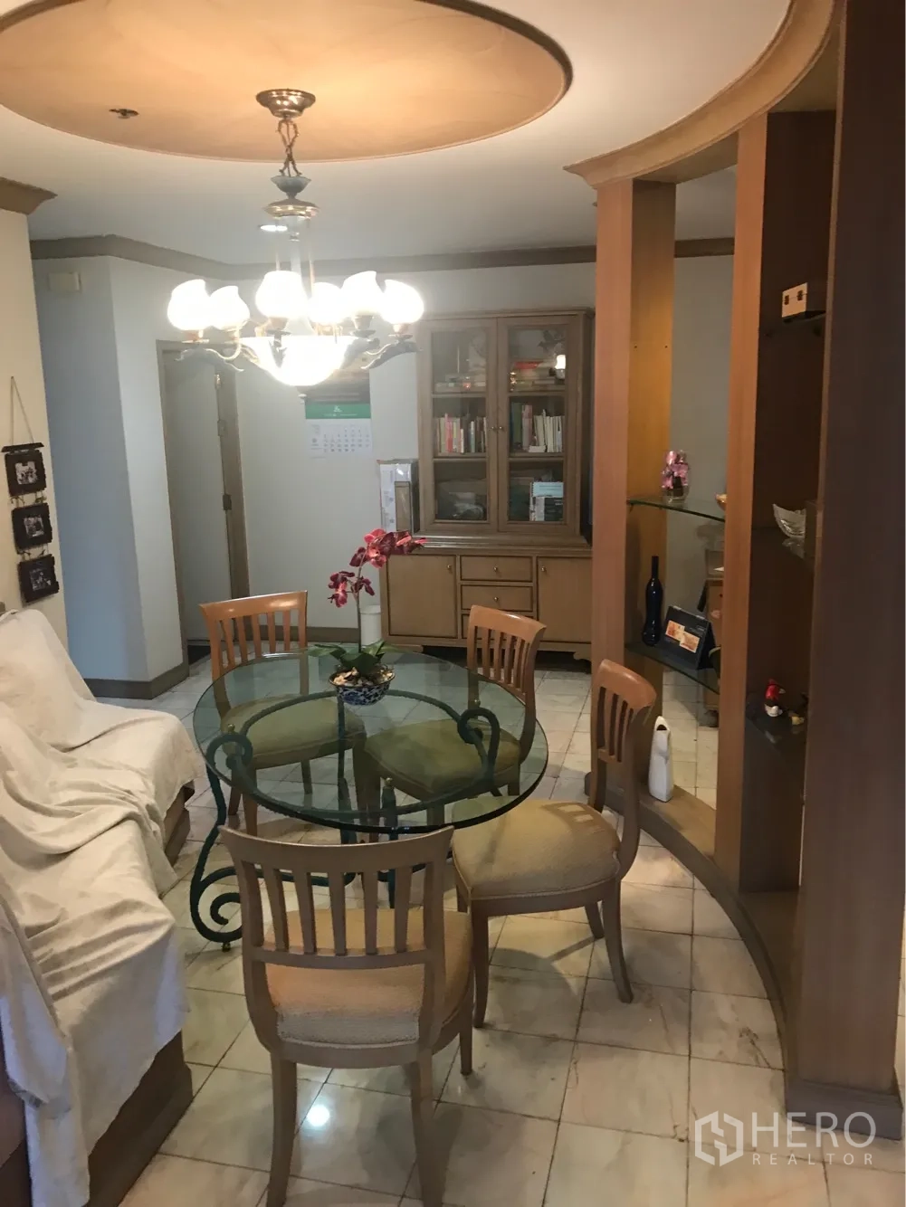 Condominium for rent or sale in Watthana, Bangkok - Dining area with a round glass table, chandelier lighting, and built-in wooden cabinetry.