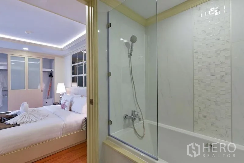 Apartment for rent in Khlong Toei, Bangkok - View from bathroom to bedroom, showing glass-partition tub and well-lit sleeping area.