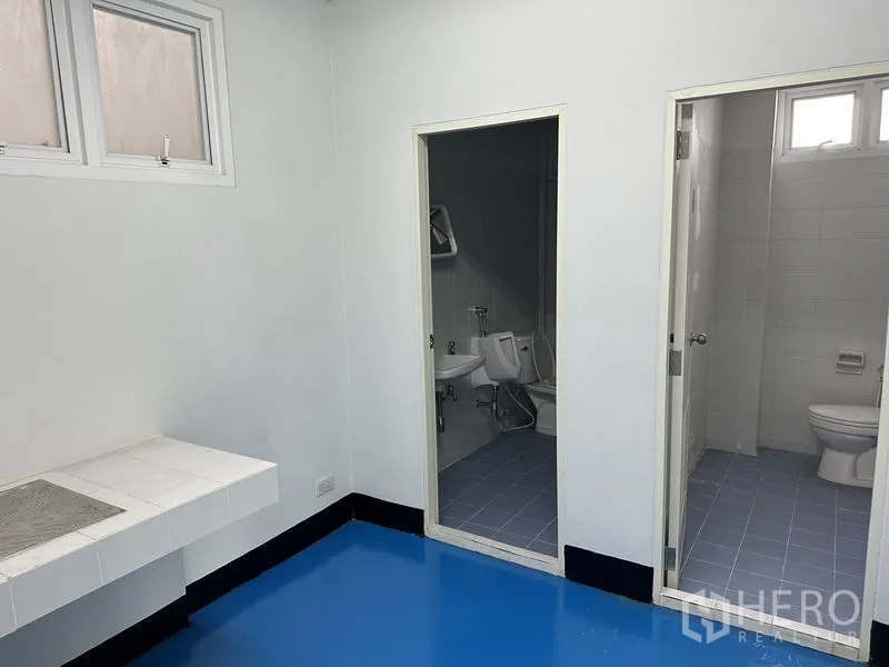 Factory for rent in Khlong Luang, Pathum Thani - Clean staff washroom area with a separate urinal room and toilet cubicle, blue epoxy floor.