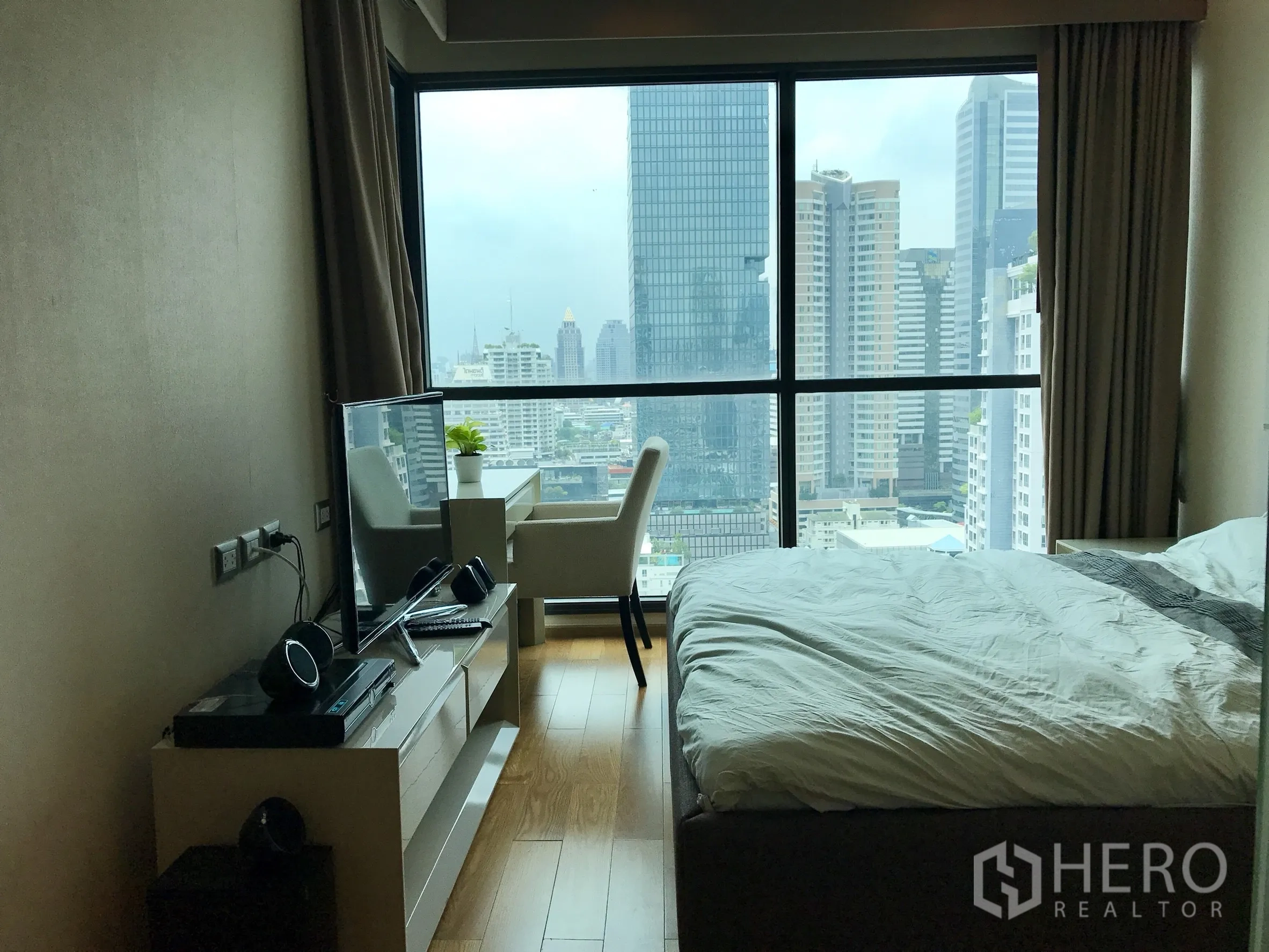 Condominium for rent or sale in Bang Rak, Bangkok - Bedroom with floor-to-ceiling windows, wood floors, desk and city view.