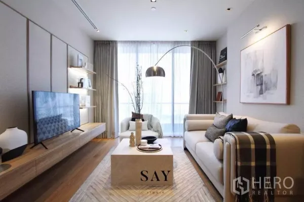 Condominium for rent or sale in Khlong Toei, Bangkok - Wide view of the living area with TV console, built‑in shelving and large windows filling the room with light.