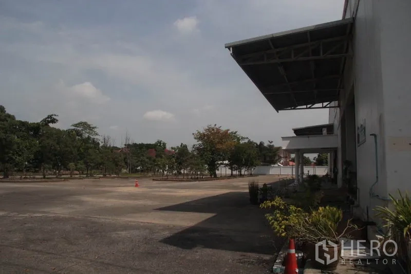 货栈 出租在Lam Luk Ka, Pathum Thani - 有遮雨棚的装卸区，面向宽敞的混凝土场地与树木。