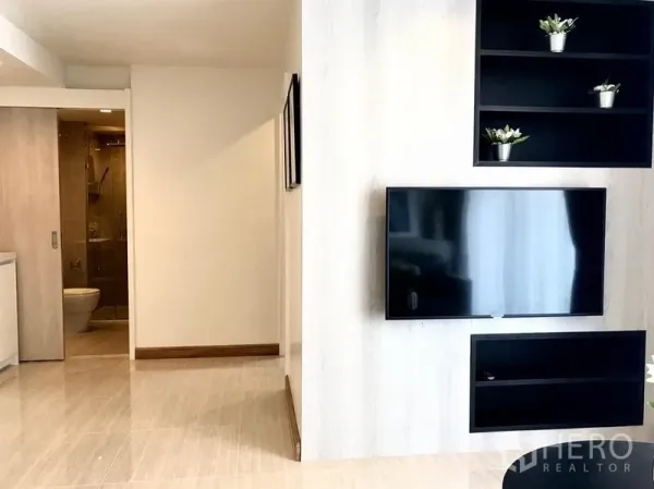公寓 出租在Watthana, Bangkok - 起居区配壁挂电视与黑色开放式层架，可见玻璃淋浴的浴室，整体极简风格。