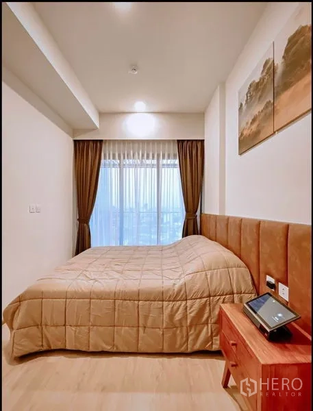 คอนโด ขายในHuai Khwang, Bangkok - ห้องนอนอบอุ่น หัวเตียงบุนวม โต๊ะข้าง และหน้าต่างบานใหญ่เห็นวิวเมือง