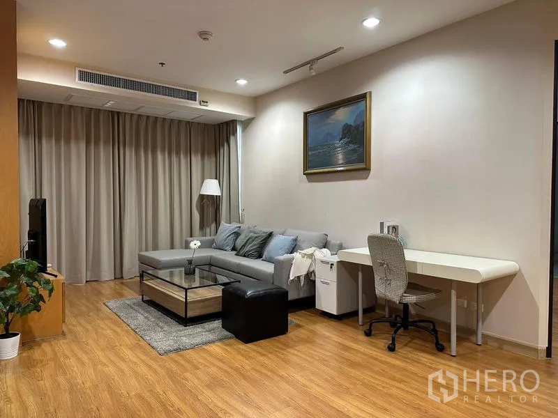 Condominium for rent in Khlong Toei, Bangkok - Open-plan lounge featuring sectional sofa, TV unit, long work desk, recessed lights and wood flooring.
