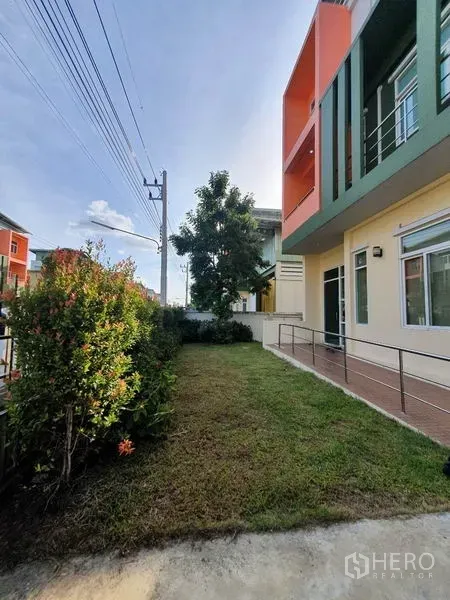 工厂 出售在Lam Luk Ka, Pathum Thani - 建筑外观，绿橙配色立面，草坪与无障碍坡道，临街绿篱。
