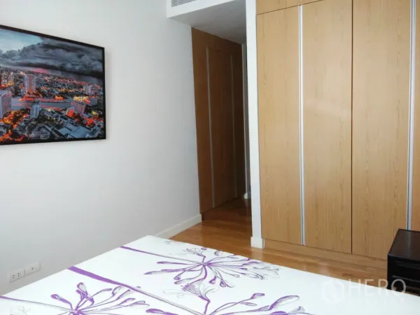 Condominium for rent in Khlong Toei, Bangkok - Bedroom with built-in wood wardrobes and cityscape artwork on the wall.