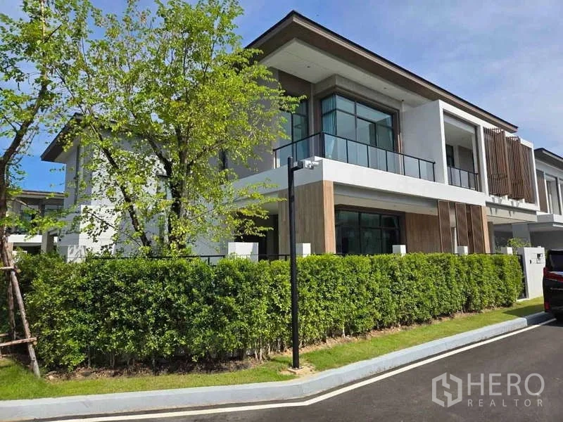 Detached House for rent in Bang Phli, Samut Prakan - Corner exterior view of a modern detached house with glass balconies and green hedges.