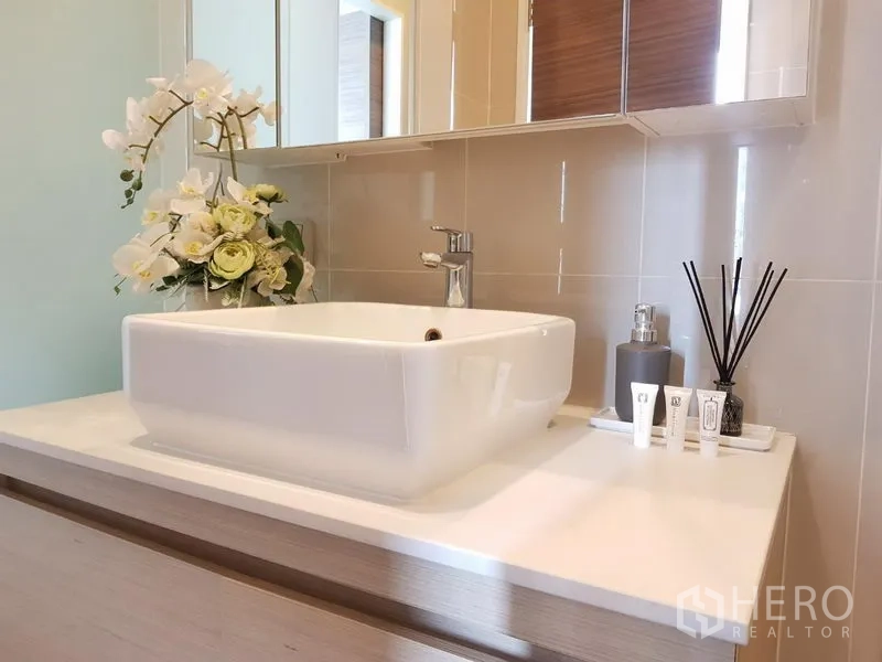 Condominium for rent in Ratchathewi, Bangkok - Contemporary bathroom vanity featuring a square basin, mirror cabinet and decorative accessories.