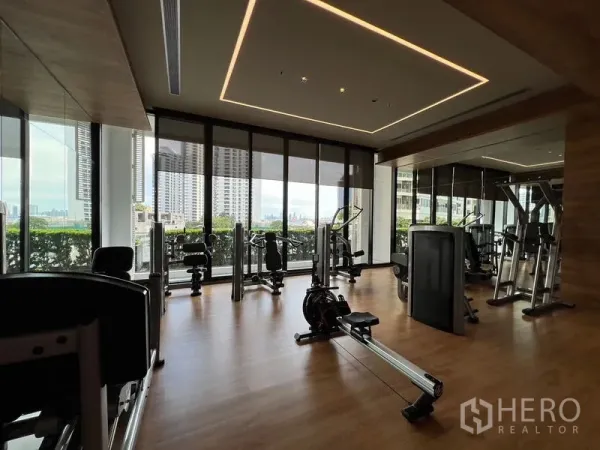 Condominium for sale - Fitness room with modern equipment, mirrors and panoramic city skyline through large windows.