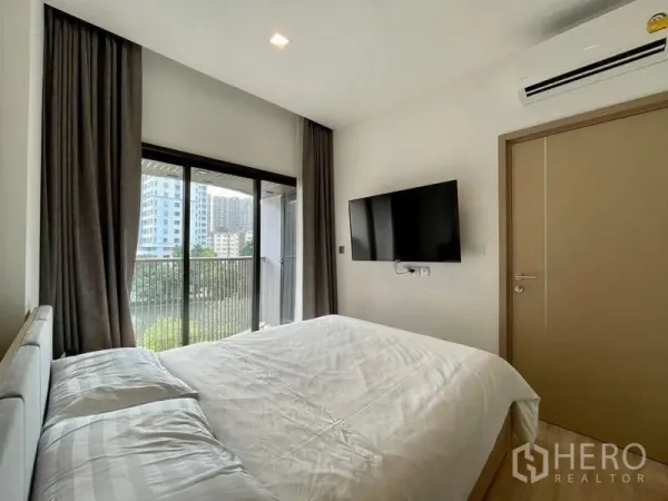 公寓 出租或出售在Watthana, Bangkok - 卧室带壁挂电视与空调，推拉门连通阳台，可见城市与绿景。