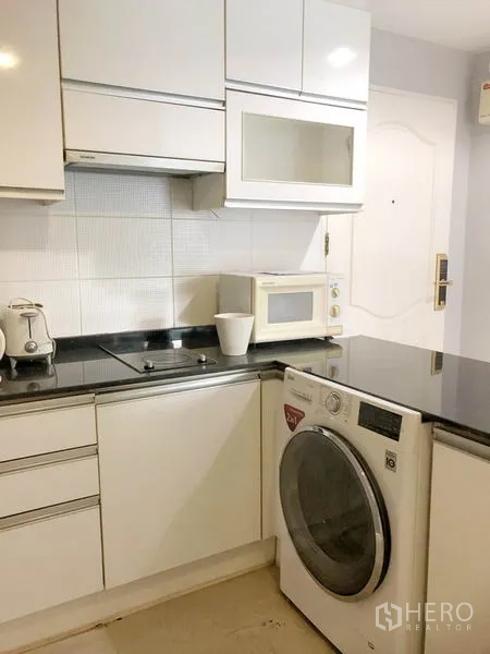 Condominium for rent or sale in Khlong Toei, Bangkok - Kitchen corner with electric cooktop, microwave and front-load washer-dryer.