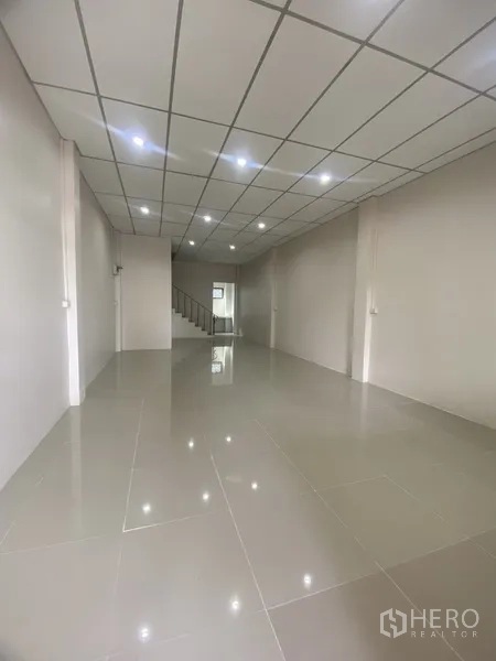 Townhouse for rent in Suan Luang, Bangkok - Spacious open-plan ground floor with glossy tiles, downlights and a staircase at the back.